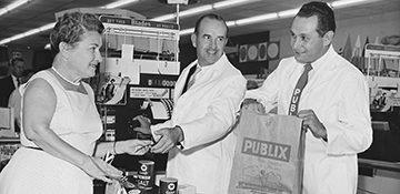 Our Founding Philosophy Image, Mr. George Jenkins and Publix Associate at the cash register assisting a customer as she checks out, black and white photo